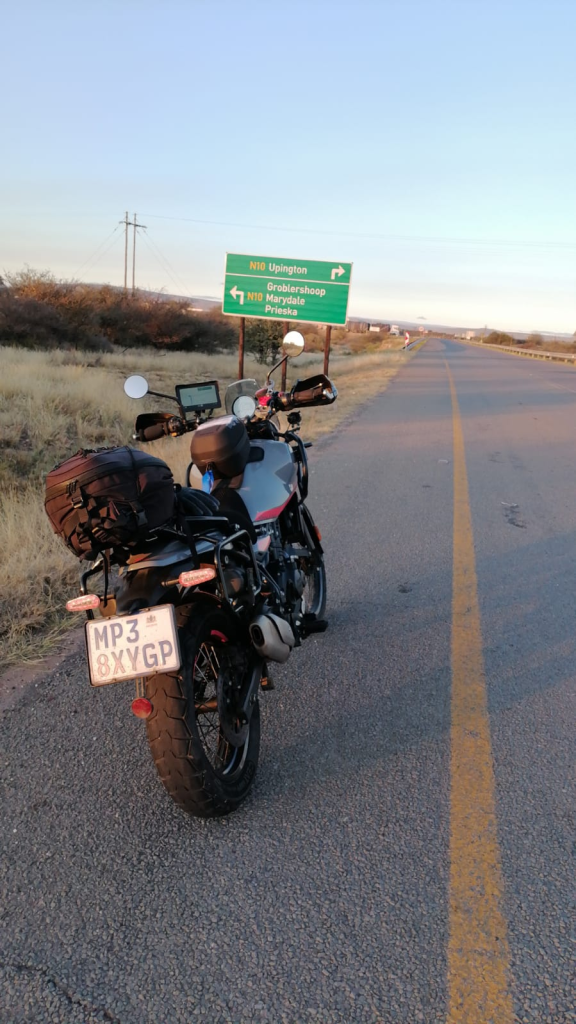 Royal Enfield Himalayan on the empty N10 at sunrise beside the sign to Upington